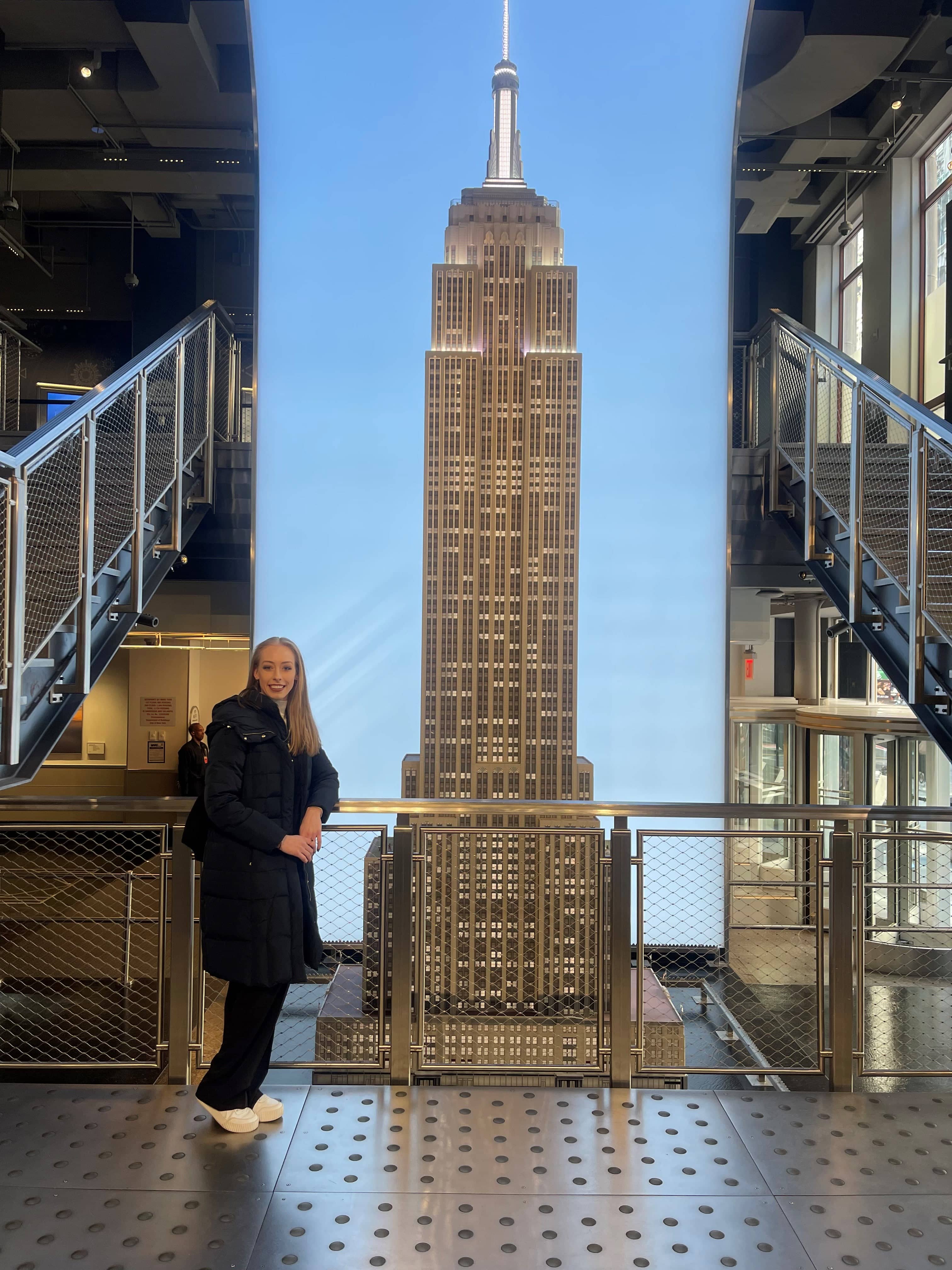 Wearing a full length black coat, Bradie Tennell stands in front of the Empire State Building.